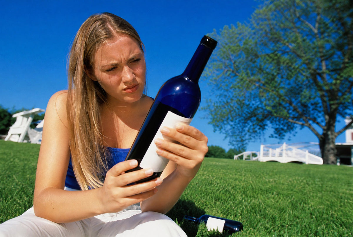 Woman closely inspecting the label of a wine bottle on a sunny lawn