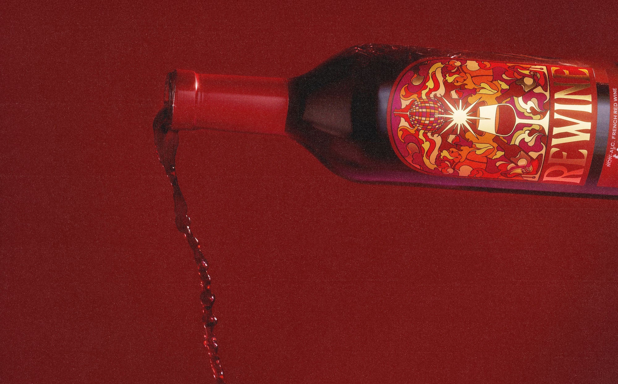 Rewine non-alcoholic Malbec pouring from a tilted bottle on a crimson backdrop
